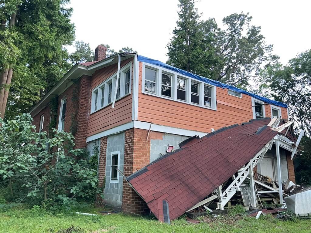 Storm-damaged roof deck and torn shingles on an Upstate SC home, with a collapsed carport-style roof overhang below